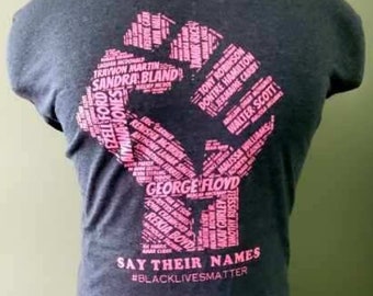 Puede incluir: Una camiseta azul oscuro con un puño rosa hecho de nombres de personas que han muerto bajo custodia policial. El texto "Say Their Names" y "#BlackLivesMatter" están impresos debajo del puño.