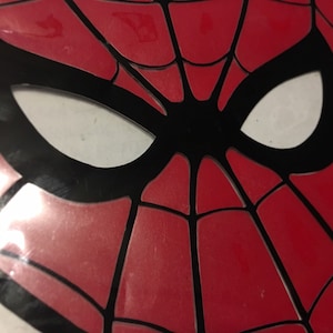 Pode incluir: Máscara do Homem-Aranha vermelha e preta com uma abertura para o olho branca.