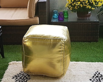 May include: An outdoor living space featuring a tan sectional sofa, a glass-top coffee table, and a gold ottoman. A cream-colored rug with black geometric patterns sits on the green turf. Potted plants and a yellow outdoor fireplace complete the scene.