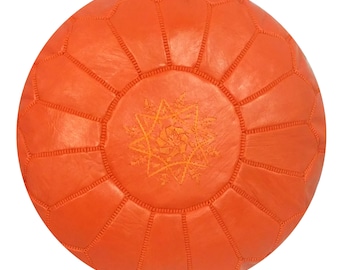 May include: Round orange leather pouf with geometric stitching and a central embroidered starburst design. This decorative ottoman is a vibrant accent piece for living rooms or bedrooms.