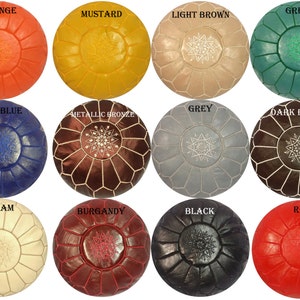 May include: A collection of round, handcrafted leather ottomans in various colors, including orange, mustard, light brown, green, navy blue, metallic bronze, grey, dark brown, cream, burgundy, black, and red. Each ottoman features a central starburst design.