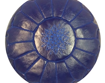 May include: A round, navy blue leather pouf with a starburst design embroidered in blue on the top. The pouf is sectioned into panels with blue stitching. The design is centered on a white background.