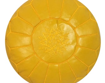 May include: A round, yellow leather pouf with a stitched geometric pattern. The center features an embroidered starburst design. The pouf is a decorative and functional piece of furniture, suitable for use as a footrest or extra seating.