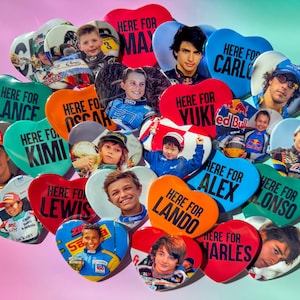 Puede incluir: Un conjunto de botones en forma de corazón con retratos de pilotos de carreras. Cada botón tiene la frase "HERE FOR" seguida del nombre de un piloto, como "MAX", "LANCE" y "CARLO". Los botones son de varios colores.