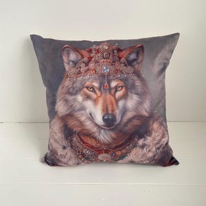 May include: Square decorative pillow featuring a regal wolf portrait. The wolf is adorned with a jeweled crown and collar, set against a gray background. The pillow has a soft, velvety texture, perfect for adding a touch of fantasy to any room.