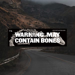 Op de afbeelding: Een zwarte sticker met de witte tekst "WARNING: MAY CONTAIN BONES" en een witte illustratie van een skelet. De afbeelding is geplaatst tegen een achtergrond van een kronkelende weg en bergen.