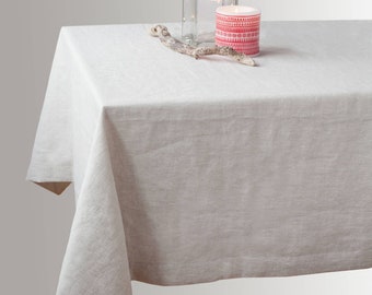 May include: A white linen tablecloth with a natural wood branch and a red and white patterned candle on top.