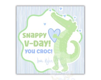 Op de afbeelding: Vierkante kaart met een lichtblauwe en witte gestreepte achtergrond. De kaart toont een groene cartoon alligator met een blauw hart. Tekst luidt "Snappy V-Day! You Croc!" in groen en blauw.