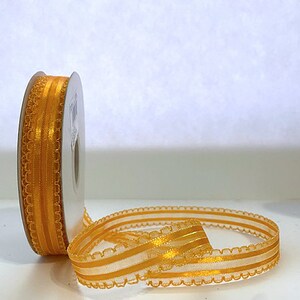 May include: A spool of gold ribbon with a scalloped edge and two thin stripes. The ribbon is made of a sheer material.