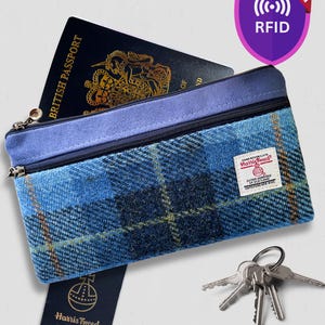 May include: A blue plaid Harris Tweed zippered pouch with a purple suede top trim, containing a British passport. The pouch features an RFID protection shield icon, a Harris Tweed fabric label, a hanging brand tag, and a set of metal keys.