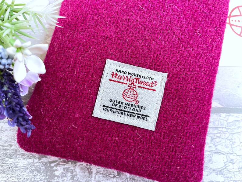 Pu&ograve; includere: Una pochette in tessuto Harris Tweed color magenta vivace con un'etichetta rettangolare bianca tessuta. L'etichetta riporta il testo HAND WOVEN CLOTH, Harris Tweed, OUTER HEBRIDES OF SCOTLAND e 100% PURE NEW WOOL, con un emblema circolare.