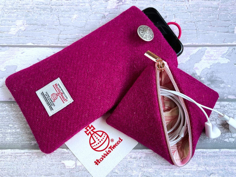 Pu&ograve; includere: Una custodia per telefono in Harris Tweed magenta con un bottone argentato e una pochette triangolare con cerniera abbinata contenente auricolari bianchi. Una carta bianca con il logo rosso Harris Tweed &egrave; posizionata sotto.