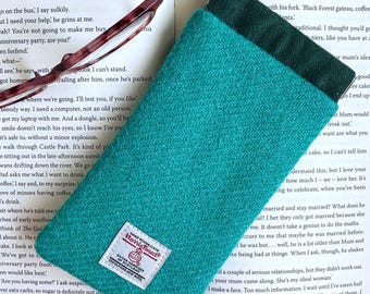 May include: A rectangular teal Harris Tweed pouch with a herringbone pattern and a dark green fabric lining. A white rectangular label with red and black text reading Harris Tweed is stitched onto the lower front of the wool pouch.