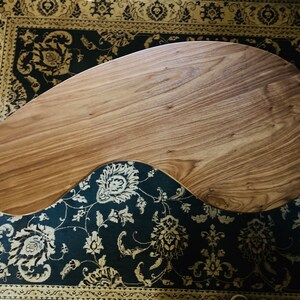 May include: A unique, free-form wooden coffee table with a natural wood finish. The table has an organic, asymmetrical shape and is resting on a patterned rug.