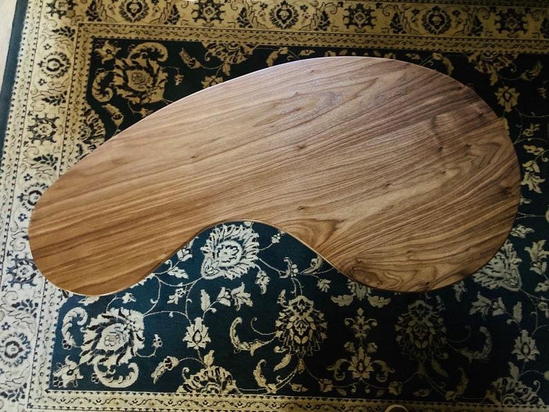 May include: A unique, free-form wooden coffee table with a natural wood finish. The table has an organic, asymmetrical shape and is resting on a patterned rug.
