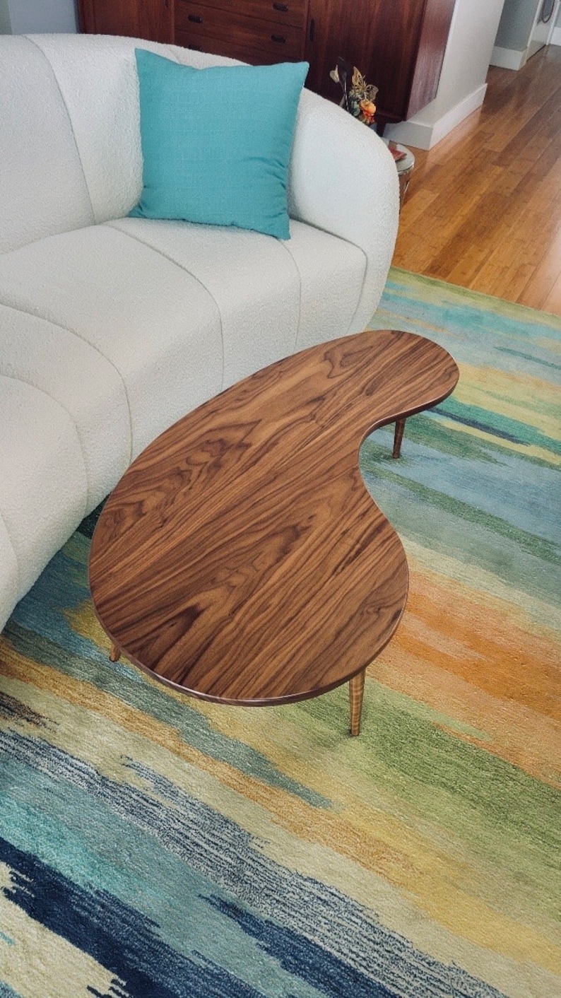 May include: A dark brown, kidney-shaped coffee table with a wood grain finish and four legs. The table is sitting on a multi-colored rug with blue, green, yellow, and orange stripes.