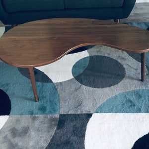 May include: A dark brown, kidney-shaped coffee table with a smooth, polished surface and two legs. The table is sitting on a blue and gray patterned rug.