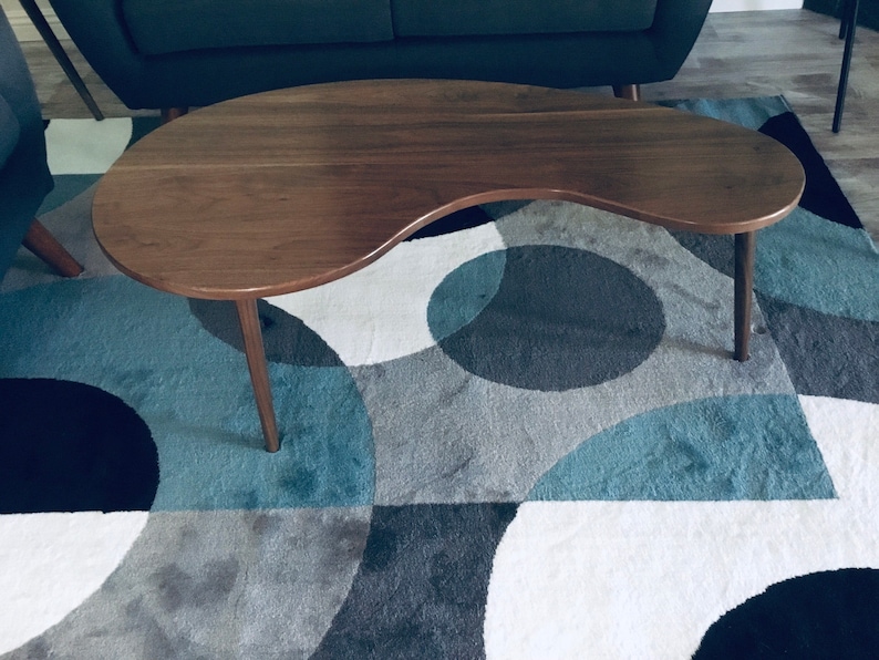 May include: A dark brown, kidney-shaped coffee table with a smooth, polished surface and two legs. The table is sitting on a blue and gray patterned rug.