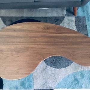 May include: A brown, oval-shaped coffee table with a smooth, wood grain surface. The table is sitting on a blue and gray patterned rug.