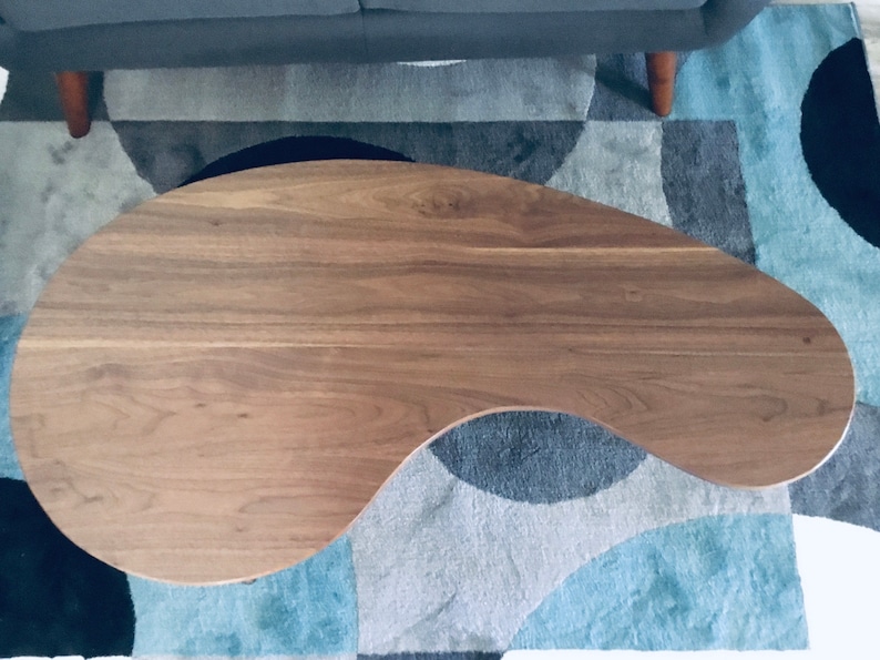 May include: A brown, oval-shaped coffee table with a smooth, wood grain surface. The table is sitting on a blue and gray patterned rug.