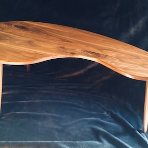 May include: A unique, free-form wooden coffee table with a natural wood finish and four slender legs. The table top has an organic, asymmetrical shape.