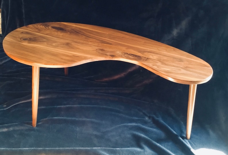 May include: A unique, free-form wooden coffee table with a natural wood finish and four slender legs. The table top has an organic, asymmetrical shape.