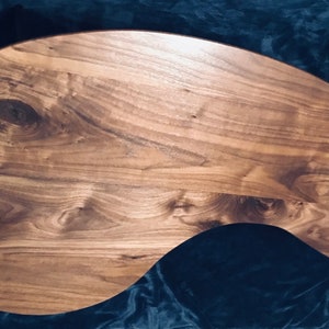 May include: A large, freeform, wooden serving tray made of walnut wood with a natural finish. The tray has a unique, organic shape and a smooth, polished surface.