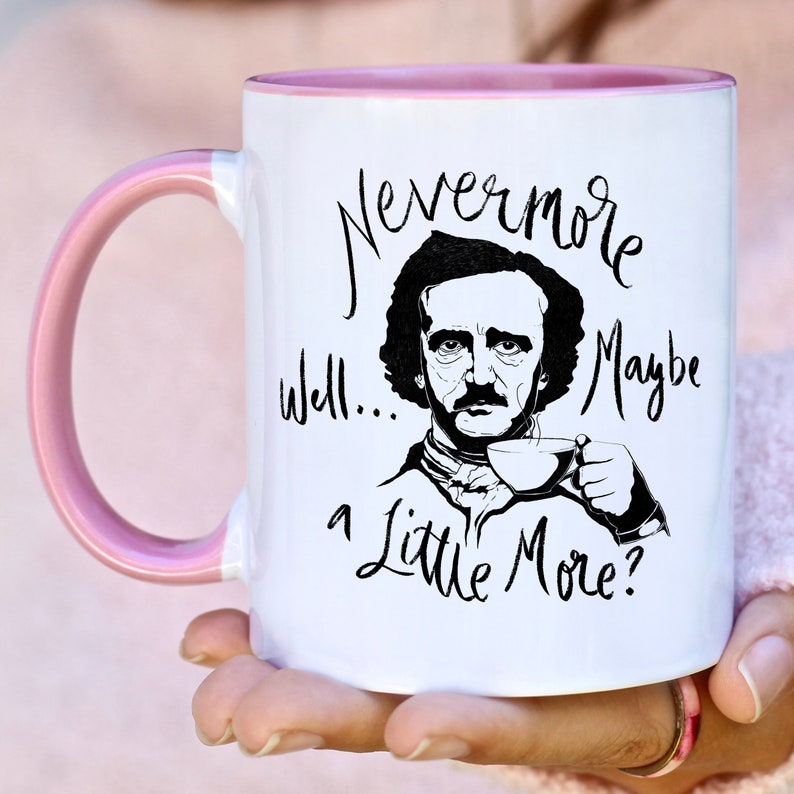 Puede incluir: Taza de caf&eacute; blanca con borde rosa. La taza presenta una ilustraci&oacute;n en blanco y negro de Edgar Allan Poe con el texto "Nevermore... well... a little more?"