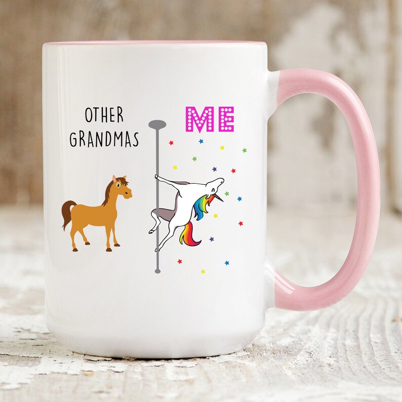 May include: White ceramic coffee mug with a pink rim and handle. The mug has a graphic of a unicorn on a pole dancing with the text "ME" above it. A brown horse is on the left side of the mug with the text "OTHER GRANDMAS" above it.