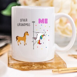 May include: White ceramic mug with a graphic of a unicorn on a pole dancing, with the text "OTHER GRANDMAS" and "ME" on either side. The unicorn is rainbow colored and has a pink mane. The background is white with small colorful stars.