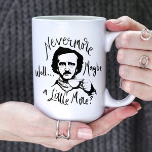 Puede incluir: Taza de caf&eacute; de cer&aacute;mica blanca con una ilustraci&oacute;n en blanco y negro de Edgar Allan Poe sosteniendo una taza de t&eacute;. La taza tiene el texto "Nevermore well... maybe a little more?" impreso en ella.