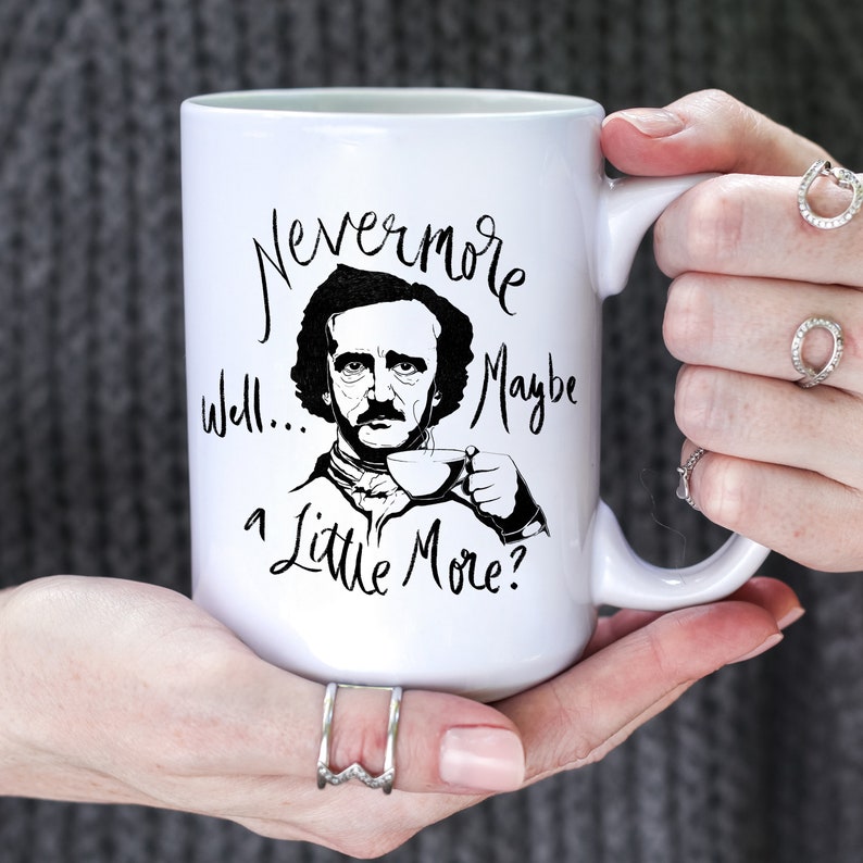 Puede incluir: Taza de caf&eacute; de cer&aacute;mica blanca con una ilustraci&oacute;n en blanco y negro de Edgar Allan Poe sosteniendo una taza de t&eacute;. La taza tiene el texto "Nevermore well... maybe a little more?" impreso en ella.