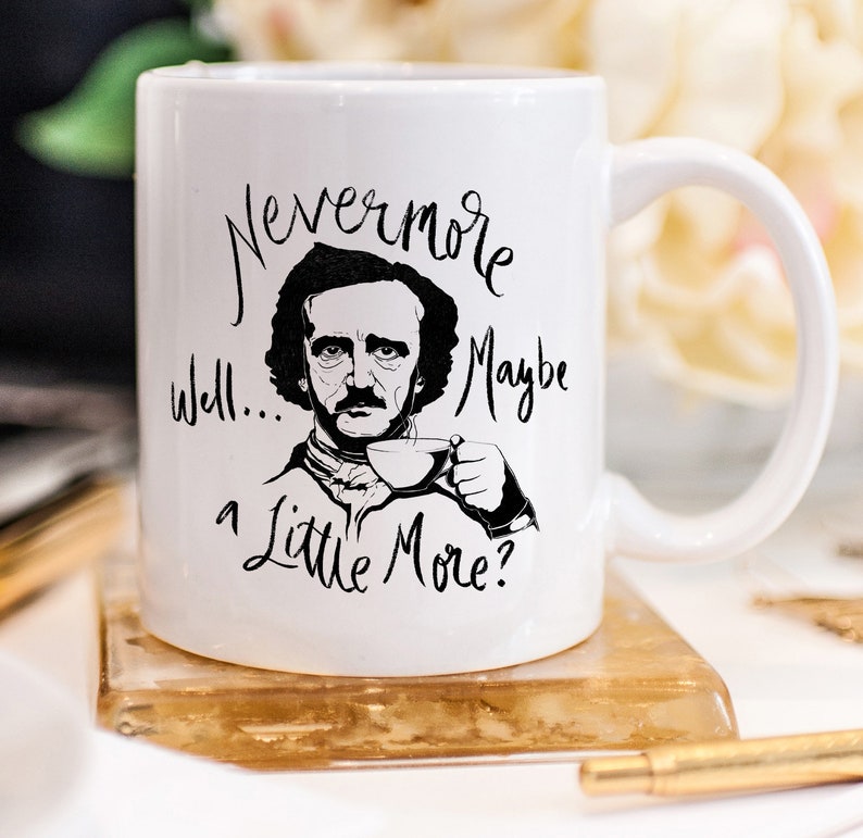 Puede incluir: Taza de cer&aacute;mica blanca con una ilustraci&oacute;n en blanco y negro de Edgar Allan Poe sosteniendo una taza de t&eacute;. La taza tiene el texto "Nevermore well... maybe a little more?" impreso en ella.