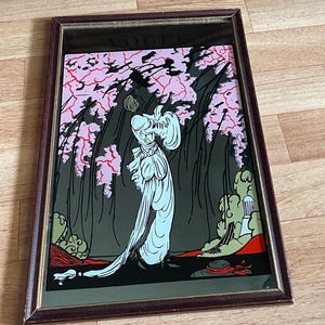May include: A framed art print featuring a woman in a flowing gown beneath pink flowering trees. The artwork is set against a dark background with green and red accents. The frame is a dark brown color.