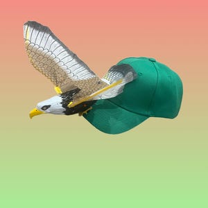 Könnte beinhalten: Eine grüne Baseballkappe mit einem Spielzeugadler, der aus der Oberseite der Kappe fliegt.