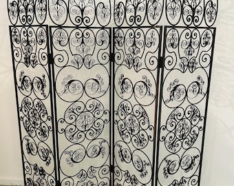 May include: A black wrought iron room divider with four panels. Each panel features intricate scrollwork and decorative oval accents. The top of the divider has ornate, stylized finials. The divider is freestanding and suitable for interior use.