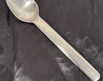 May include: A silver spoon with a long handle and an oval bowl. The spoon is made of a shiny metal and is set against a dark background. The spoon is likely for eating or serving food.