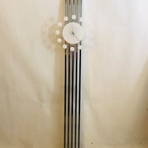 May include: A modern chrome clock with a white face and clear acrylic circle around the clock face. The clock is hanging on a white wall.