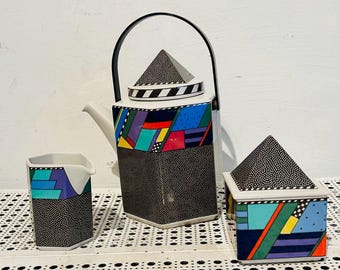 May include: A geometric tea set featuring a teapot, creamer, and sugar bowl. The teapot has a black handle and lid with a pyramid-shaped finial. The set is decorated with colorful geometric patterns and a black dotted texture.