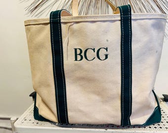 May include: A cream-colored canvas tote bag featuring dark green fabric handles and a matching dark green base. The letters BCG are embroidered in dark green thread on the front center of the bag. The bag has visible white stitching.