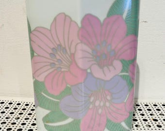 May include: White ceramic vase with a hexagonal shape, adorned with a floral design in shades of pink, purple, and green. The flowers are stylized and arranged on the front of the vase, creating a decorative accent.