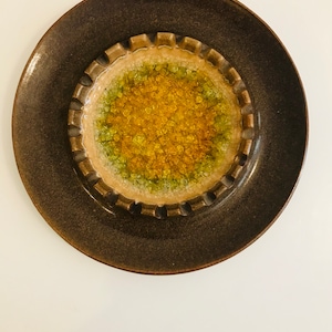 May include: A brown ceramic ashtray with a scalloped edge and a yellow and green center. The center is made of small, textured pieces of glass.