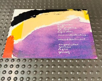 May include: A rectangular print featuring abstract brushstrokes in black, yellow, orange, and purple. The text reads: Compassion is not just something you have to give others but an understanding attached detachment empathy that you have to give yourself.