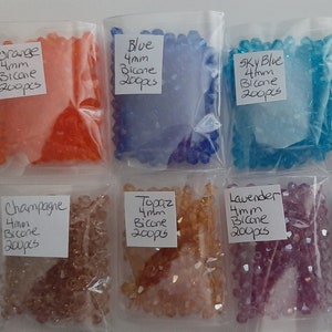 May include: Eight small plastic bags filled with 4mm bicone beads in various colors: orange, blue, sky blue, clear, champagne, topaz, lavender, and mixed. Each bag has a label with the color and "4mm Bicone 200pcs".