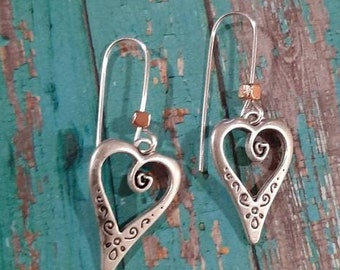 May include: A pair of silver heart-shaped earrings with intricate designs. The earrings have a dangling design with a small bead at the top of the earring.