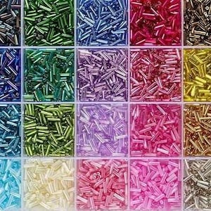 May include: A variety of colorful seed beads in a divided storage container. The beads are in shades of black, blue, green, purple, red, gold, and more. These small, cylindrical beads are used for jewelry making and crafts.