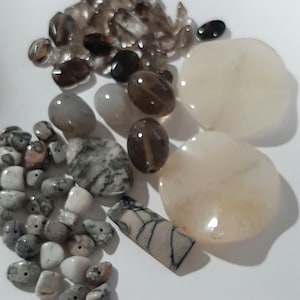 May include: A collection of various natural stones and crystals, including clear quartz, smoky quartz, agate, and jasper. The stones are in various shapes and sizes, and some have a natural, rough texture.
