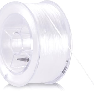 May include: A spool of clear, transparent fishing line. The line is tightly wound around a clear plastic spool. The spool has a circular shape with a central hub and a clear, thin line extending from the spool.