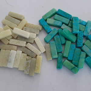 May include: Assortment of rectangular shaped gemstone beads in various colors, including brown, white, and blue-green. The beads are arranged in four groups on a white surface.