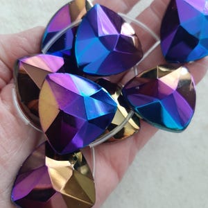May include: Iridescent, faceted teardrop-shaped beads in shades of purple, blue, and gold. The beads have a geometric design and are strung together. These beads are suitable for jewelry making and craft projects.